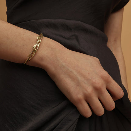 Gold bracelet on a wrist with a plain background