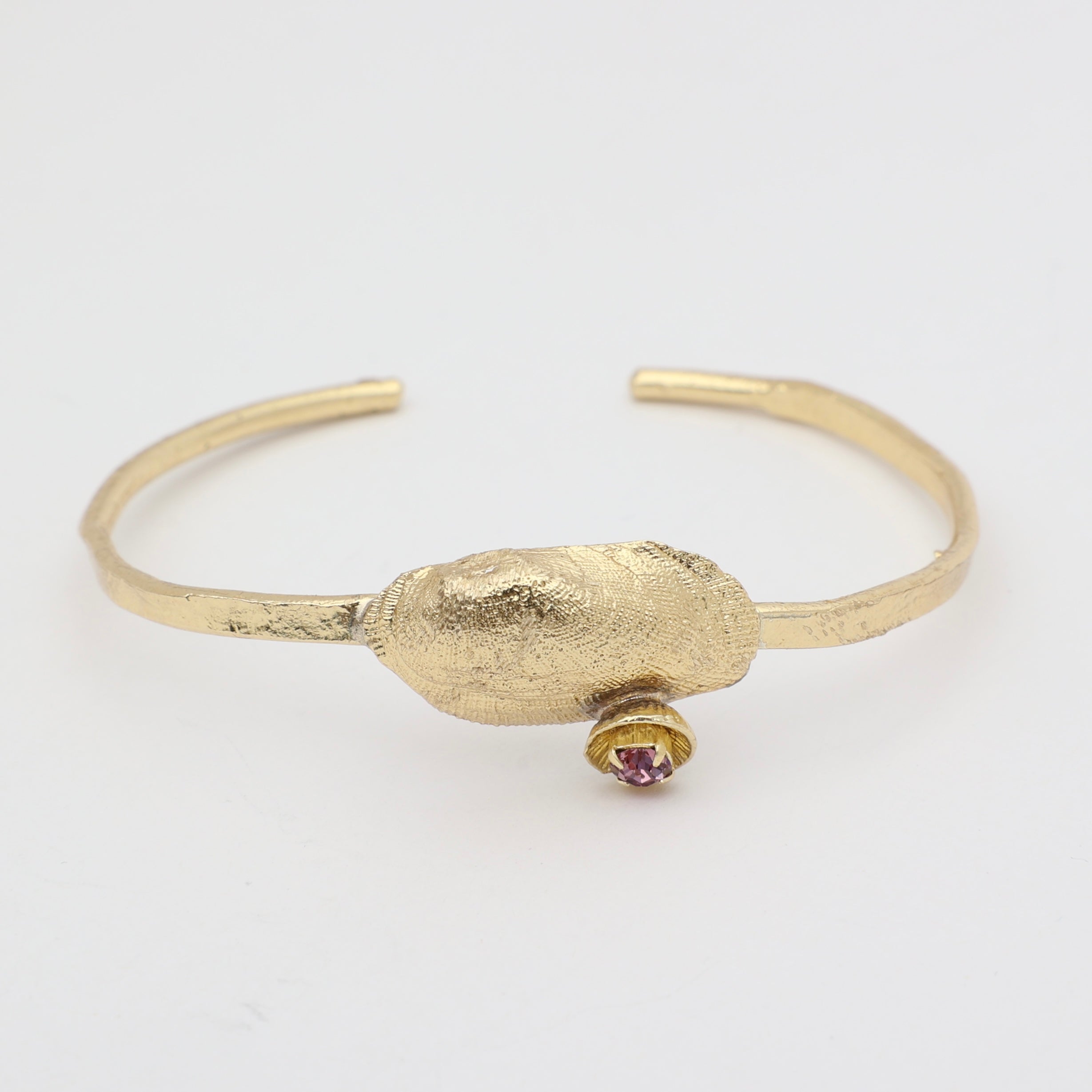 handmade brass open cuff with textured shell centerpiece and crystal detail on white background
