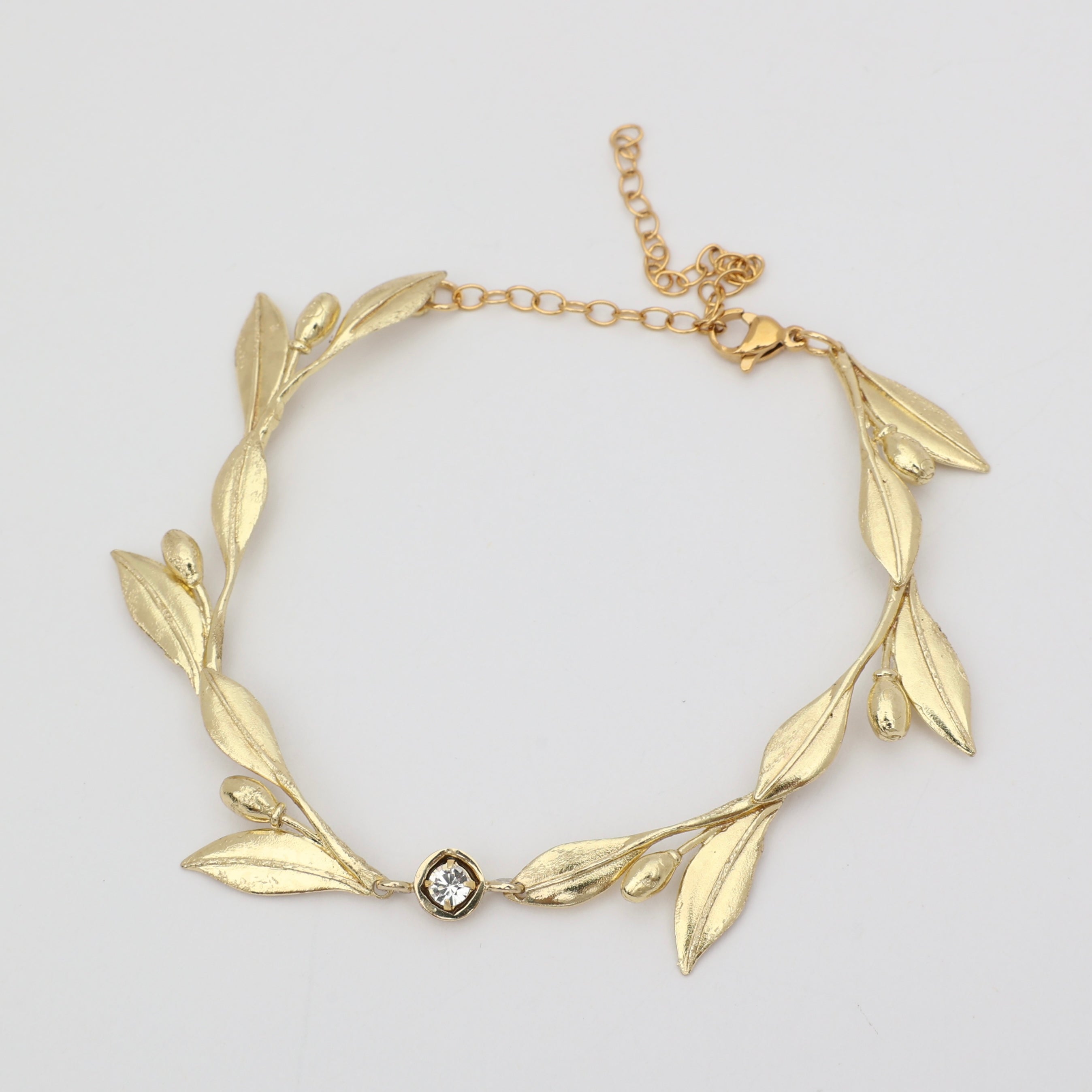 Handmade brass sculptural leaf bracelet with crystal accent on white background
