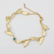 Handmade brass botanical branch bracelet with bezel-set crystal centerpiece, flat lay

