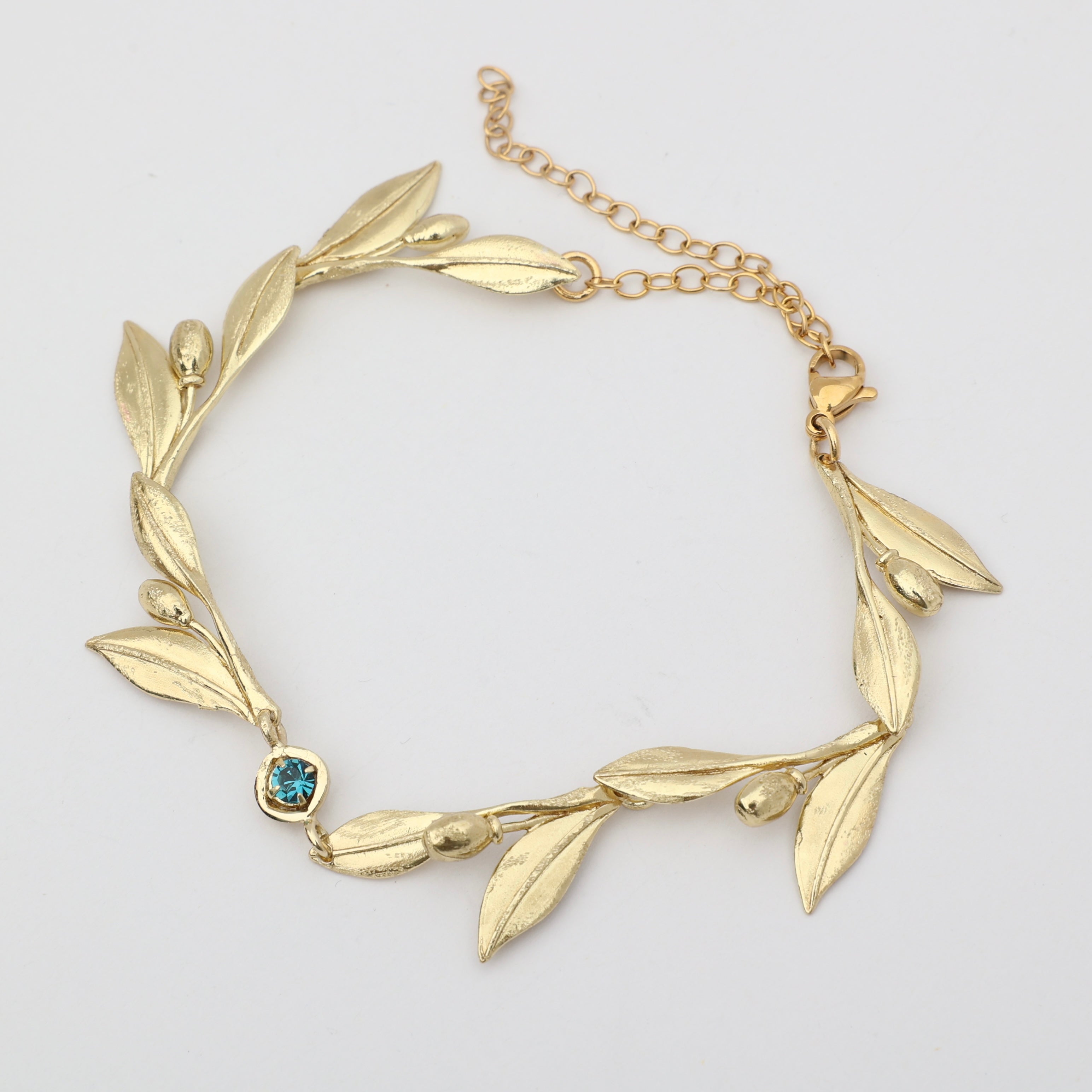 Handmade brass botanical branch bracelet with bezel-set crystal centerpiece, flat lay
