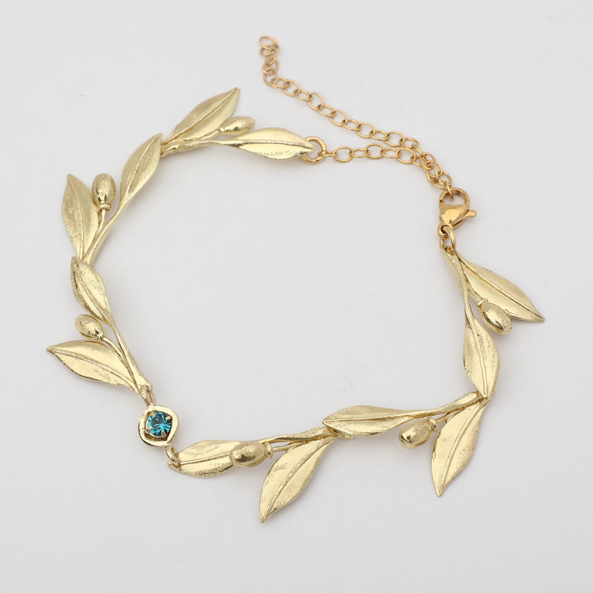 Handmade brass botanical branch bracelet with bezel-set crystal centerpiece, flat lay
