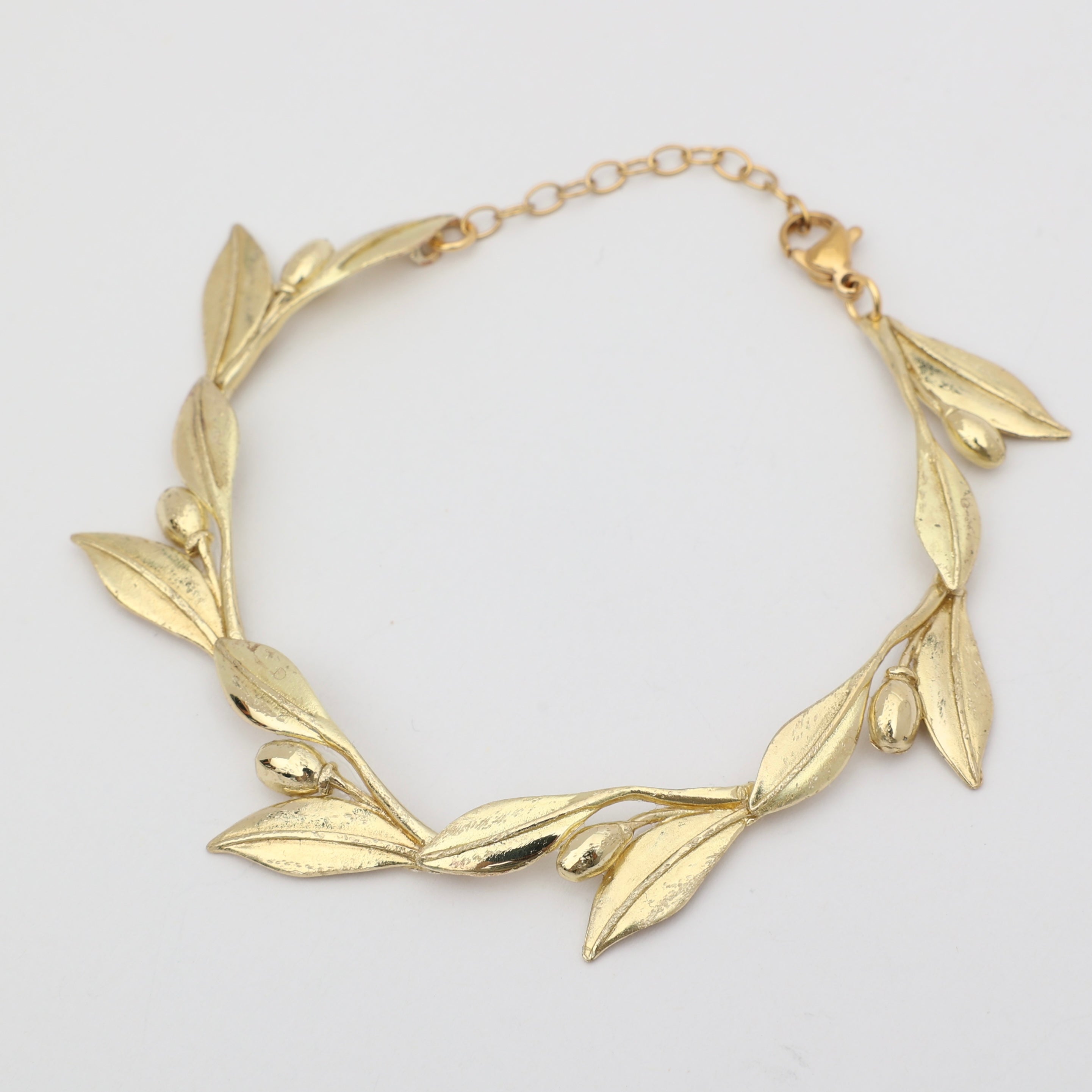 Handmade brass sculptural leaf and fruit bracelet on white background
