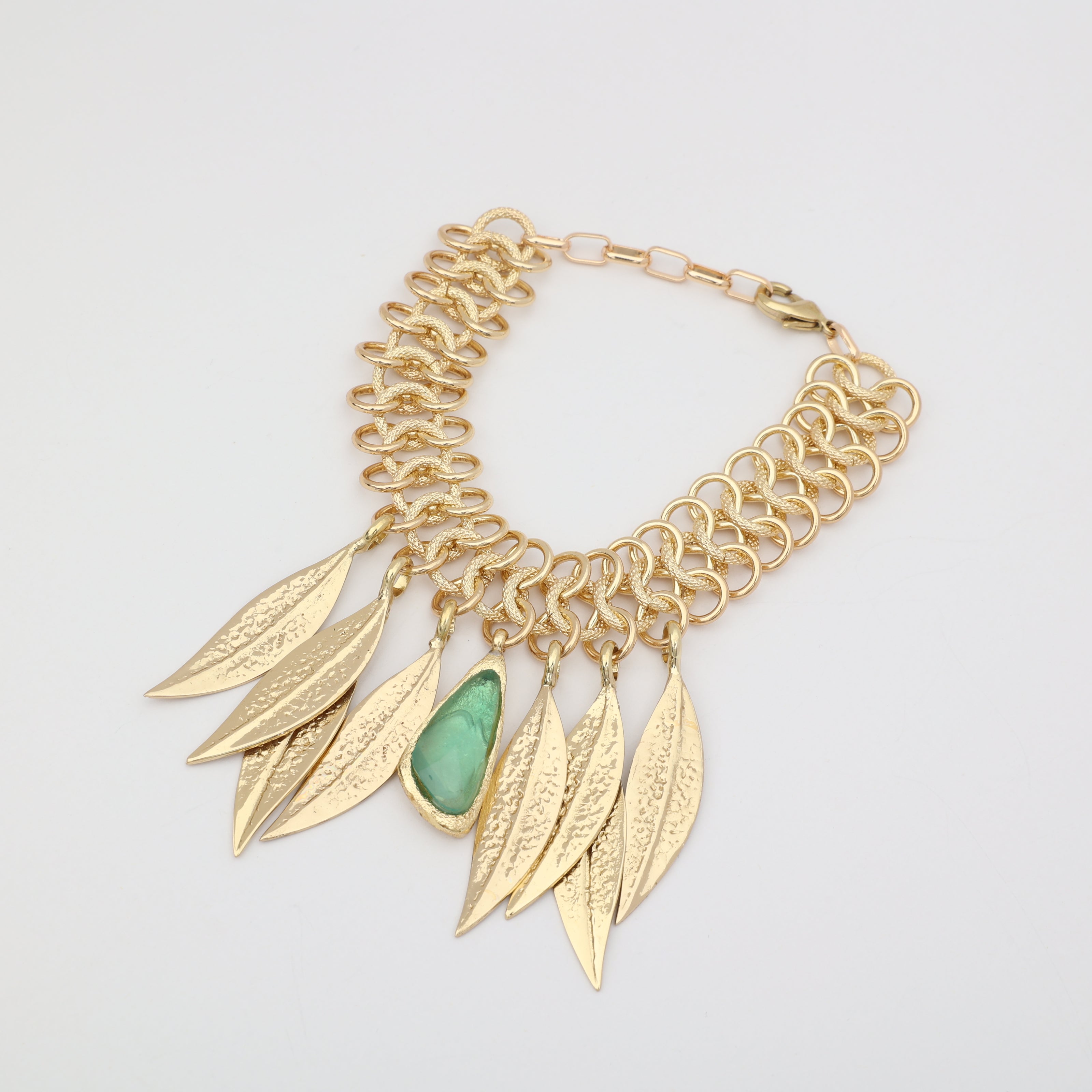 Handmade brass chainmail bracelet with sculptural leaf charms and resin stone on white background
