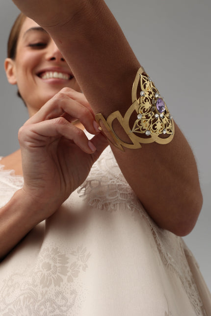 Close-up of a woman putting on a luxurious brass filigree cuff bracelet.