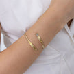 Woman wearing the Glade gold open cuff bracelet with textured leaf-shaped ends and a baguette crystal,