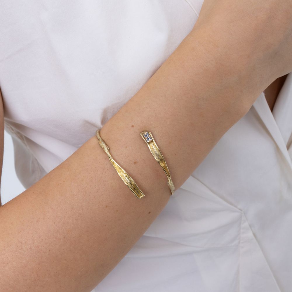 Woman wearing the Glade gold open cuff bracelet with textured leaf-shaped ends and a baguette crystal,