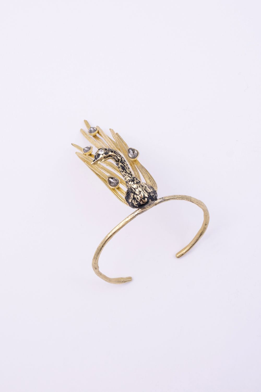 Gold peacock cuff bracelet with black oxidized bird and grey crystal feather tips, angled view on white background