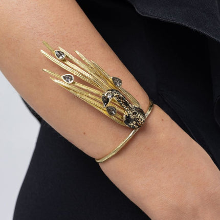 Woman wearing the gold Peacock cuff bracelet with black oxidized bird and smoky grey teardrop crystals