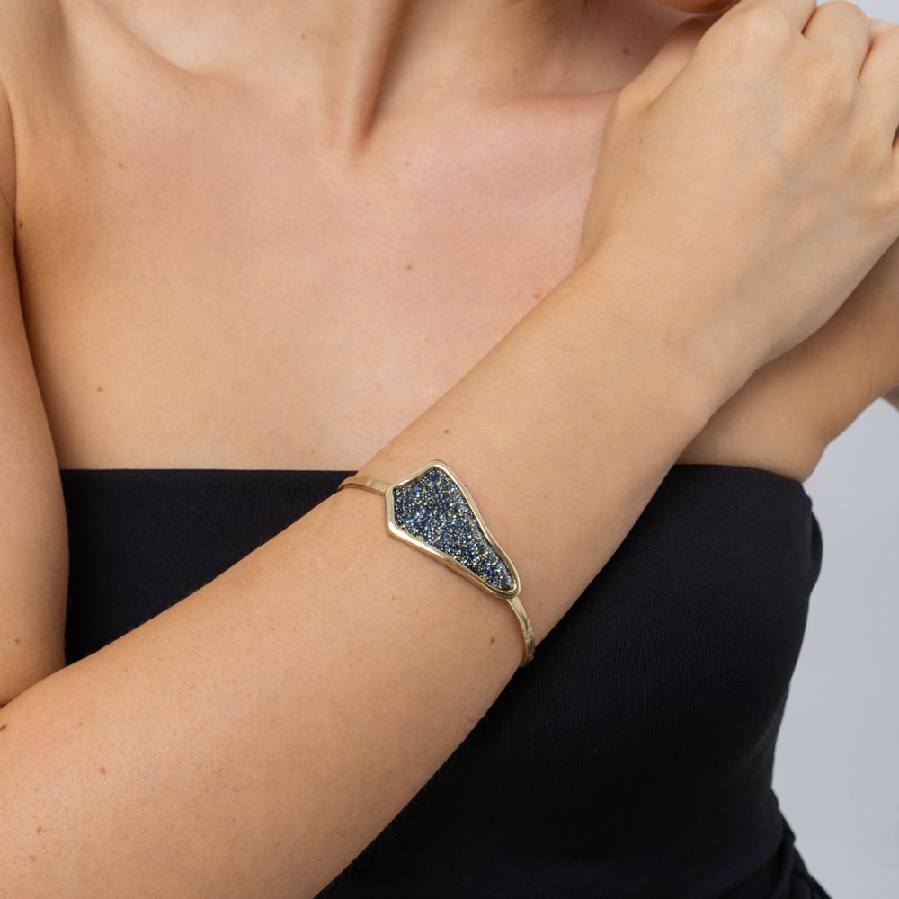 Woman wearing the Edge gold-plated cuff bracelet with a sculptural plate of iridescent blue crystals, Glitter Kiss