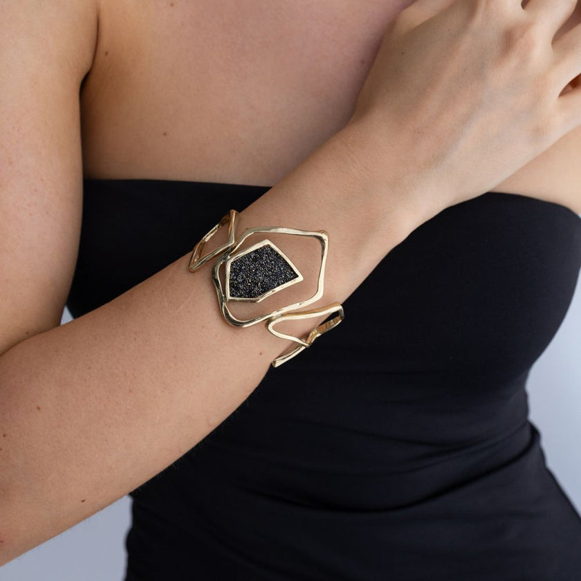 Woman wearing handmade sculptural gold cuff with open geometric lines and crystal panel, Glitter Kiss collection