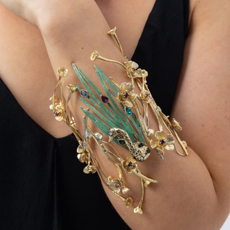 Woman wearing the Plume peacock statement cuff bracelet with golden branches, flowers, green patina feathers and colorful crystals