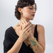 Model wearing the Plume peacock cuff bracelet with matching gold flower earrings, necklace and ring from the Savage Flora collection
