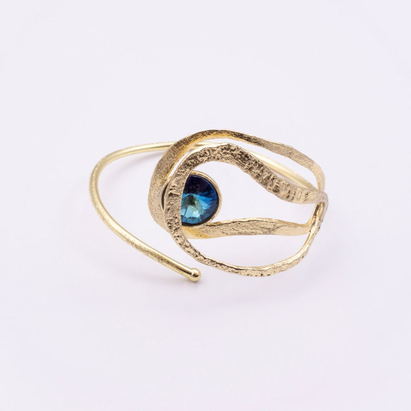 Boteh gold wrap cuff bracelet with textured leaf-like loops and iridescent blue crystal, angled view on white background
