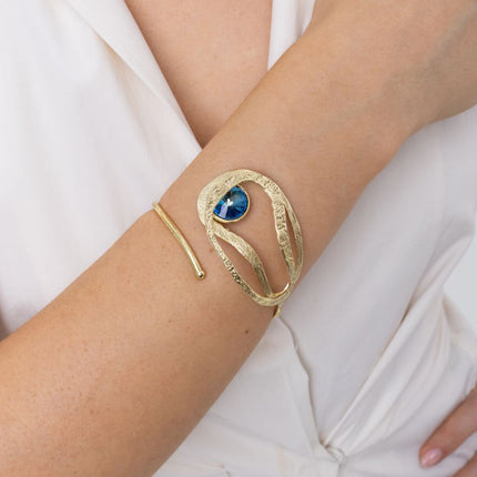Woman wearing the Boteh nature-inspired gold cuff bracelet with a blue crystal, Savage Flora