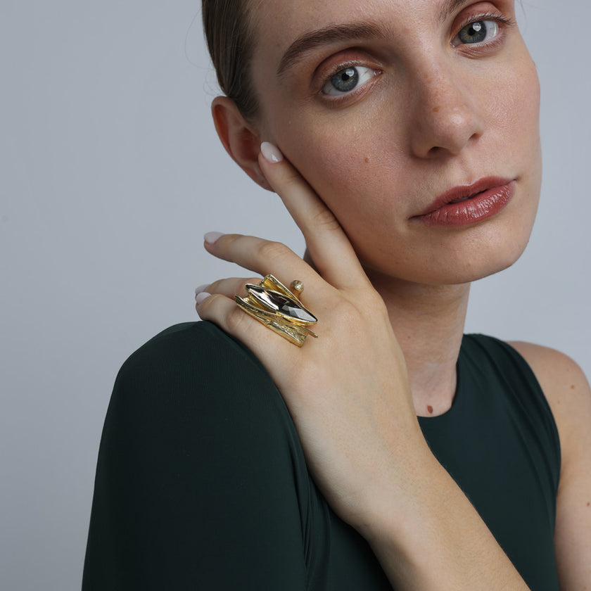 Handmade gold-tone brass sculptural cocktail ring with large marquise grey crystal and layered petal design worn on hand — Dazzle Ring by Kalliope Jewelry, crafted in Greece