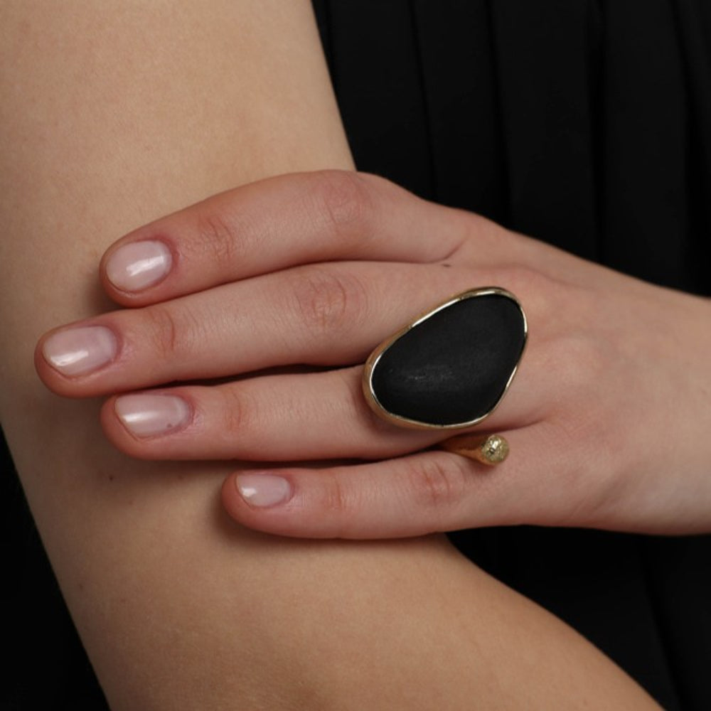 Elemental Pebble Ring close-up — handmade brass frame holding a smooth raw resin stone