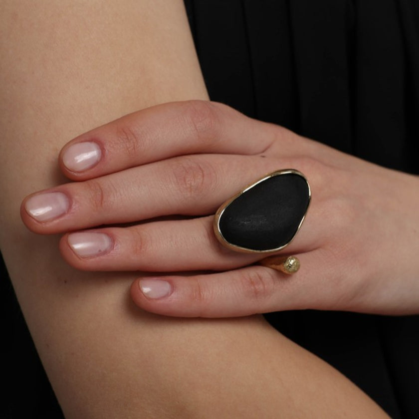 Elemental Pebble Ring close-up — handmade brass frame holding a smooth raw resin stone