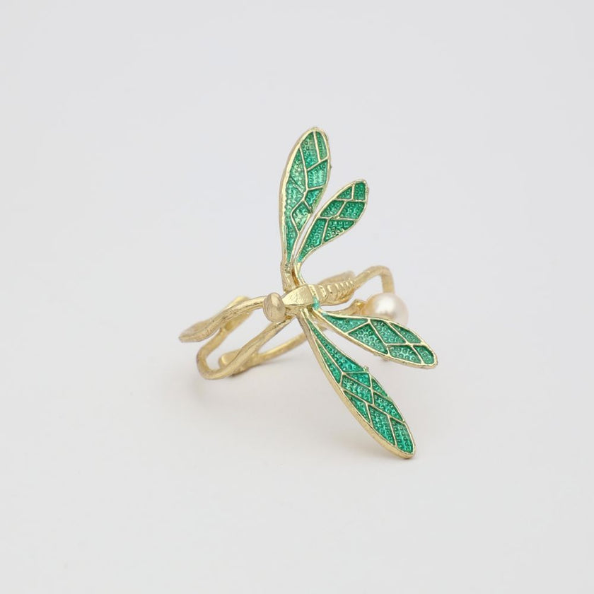 Gold ring with green dragonfly design on a light gray background