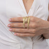 Woman wearing the Pine gold-plated brass statement ring with layered needle-like bands across two fingers, Savage Flora