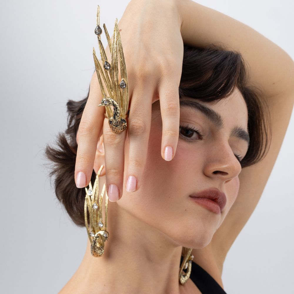 Model wearing the gold Peacock statement ring with black oxidized bird and smoky crystal feathers, with matching peacock earrings, Savage Flora