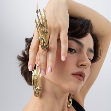 Model wearing the gold Peacock statement ring with black oxidized bird and smoky crystal feathers, with matching peacock earrings, Savage Flora