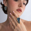 Close-up of sculptural gold ring with compressed crystal panel and matching crystal earring