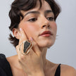 Woman wearing sculptural gold oval ring with crystal panel, hand resting on the cheek