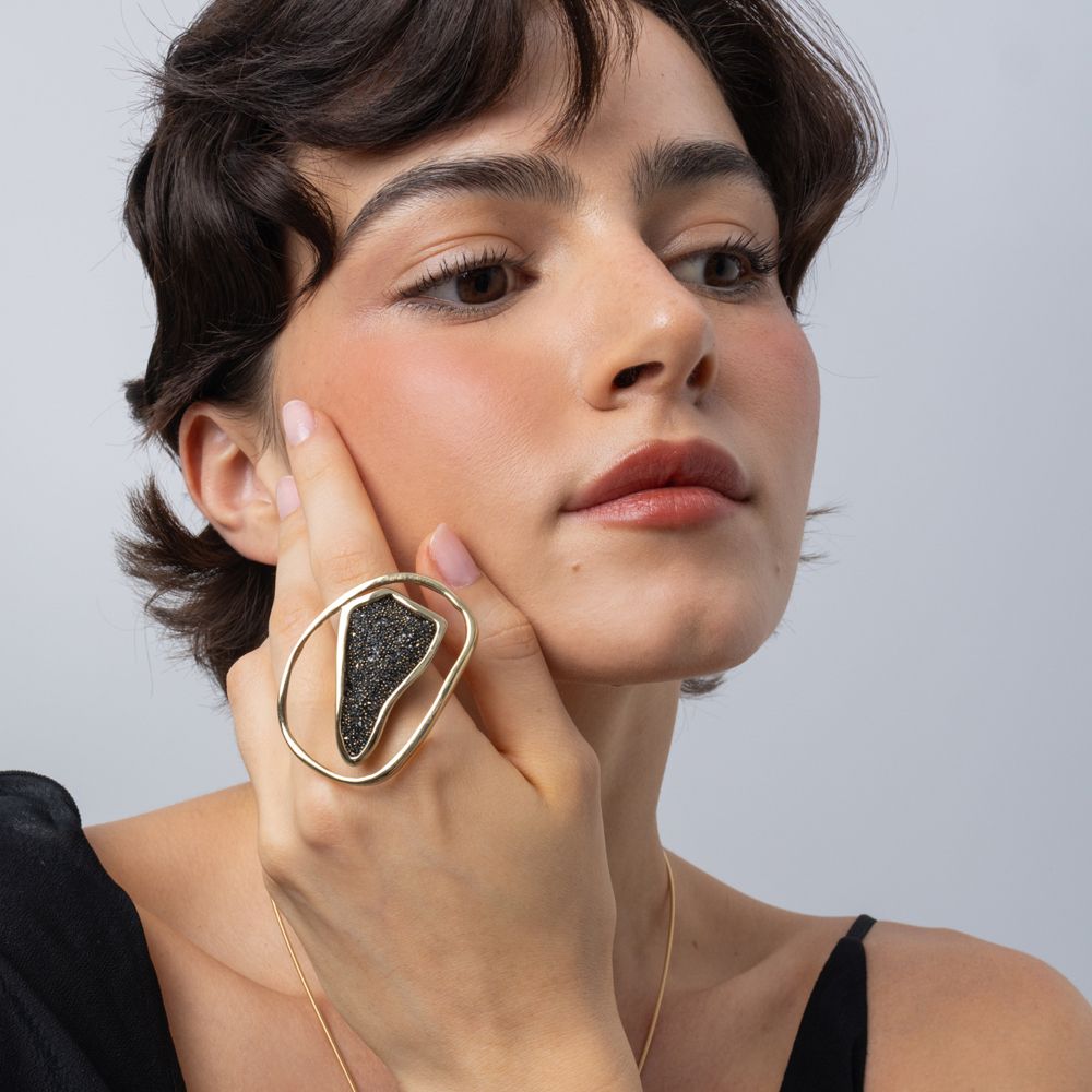 Woman wearing sculptural gold oval ring with crystal panel, hand resting on the cheek