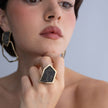 Woman wearing handmade geometric crystal ring with angular gold frame, resting hand under the chin