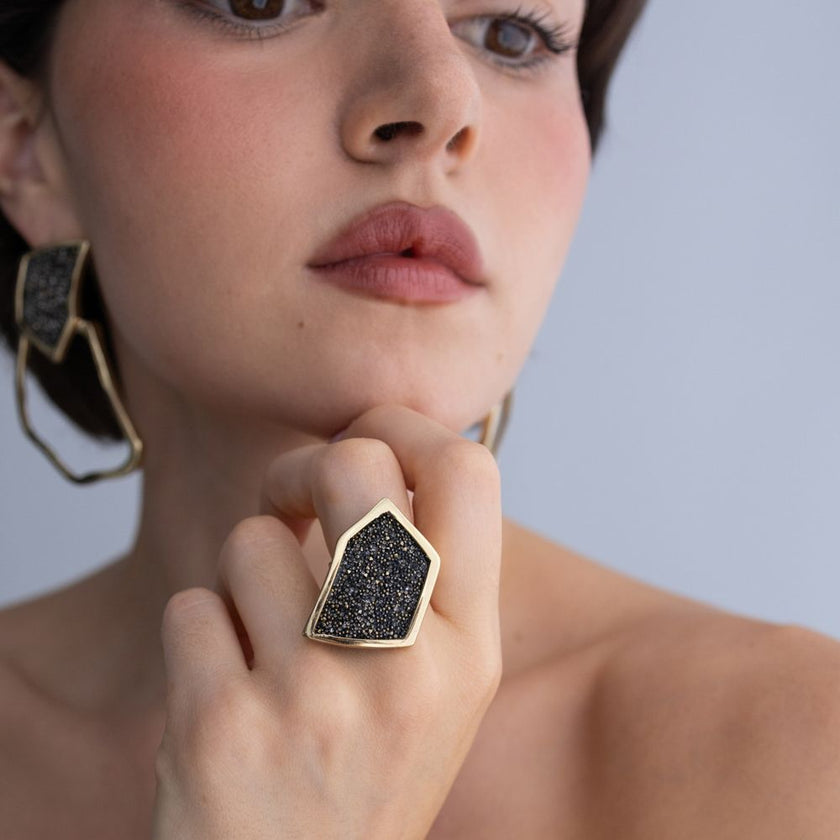 Woman wearing handmade geometric crystal ring with angular gold frame, resting hand under the chin