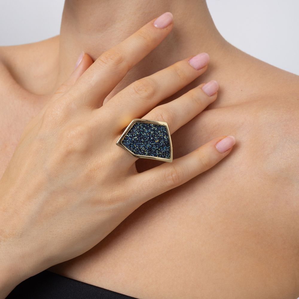 Close-up of sculptural gold ring with faceted crystal panel on the middle finger