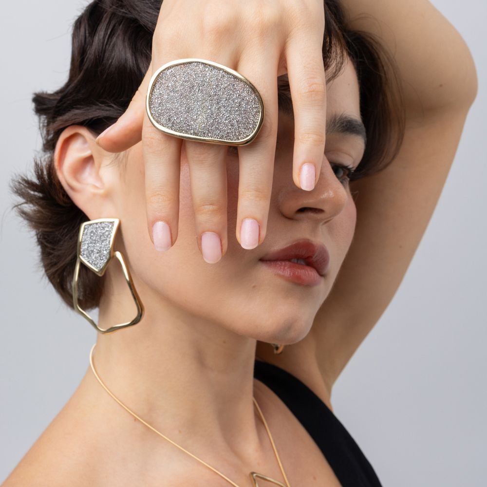 Model wearing Glitter Kiss oval crystal ring with matching geometric crystal earrings and gold necklace