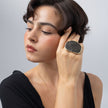 Model with large sculptural gold oval ring covered in compressed crystals, hand resting at the temple