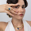 Shiny Boteh gold-plated brass statement ring with iridescent blue crystal and layered textured bands, angled view on white background