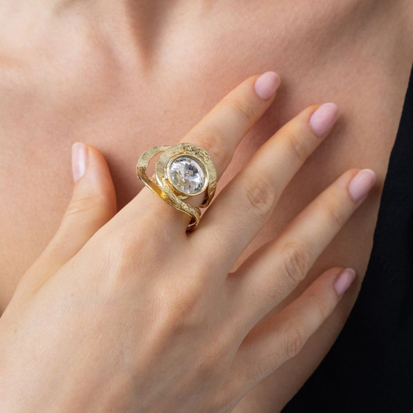 Woman wearing the Shiny Boteh gold cocktail ring with a large clear round crystal and sculptural loops, Savage Flora