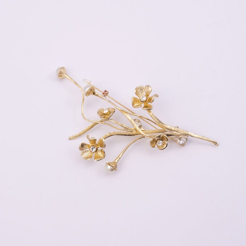 Brass floral pin with pearl-tipped stems and crystal blooms, flat lay