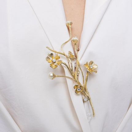 Brass flower pin with pearl buds and colored crystals worn on lapel