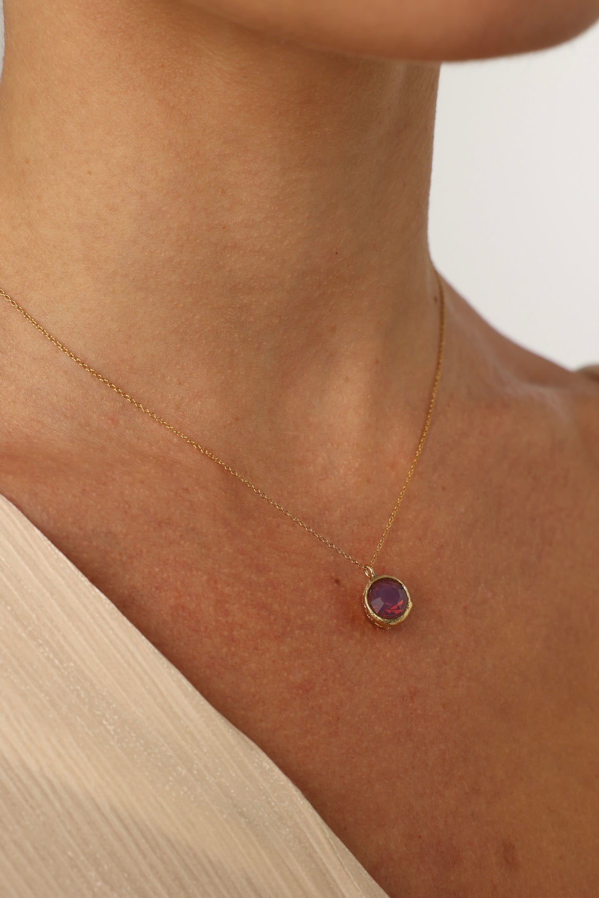 Necklace with a purple gemstone pendant on a person's neck against a neutral background