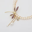Pearl necklace with a dragonfly charm on a light gray background