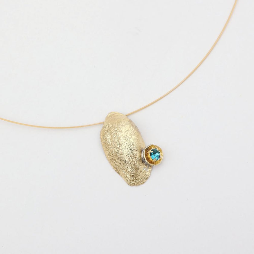 Gold necklace with a textured pendant and blue gemstone on a white background