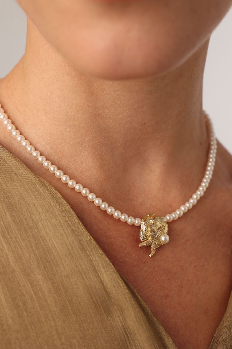 Tide Necklace close-up — artisan brass sea charm on a pearl necklace