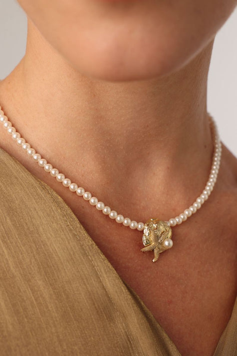 Tide Necklace close-up — artisan brass sea charm on a pearl necklace