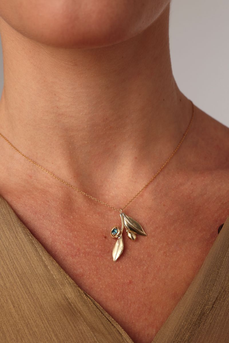 Alea Necklace flat lay — handmade brass botanical pendant necklace with bezel-set crystal olive detail
