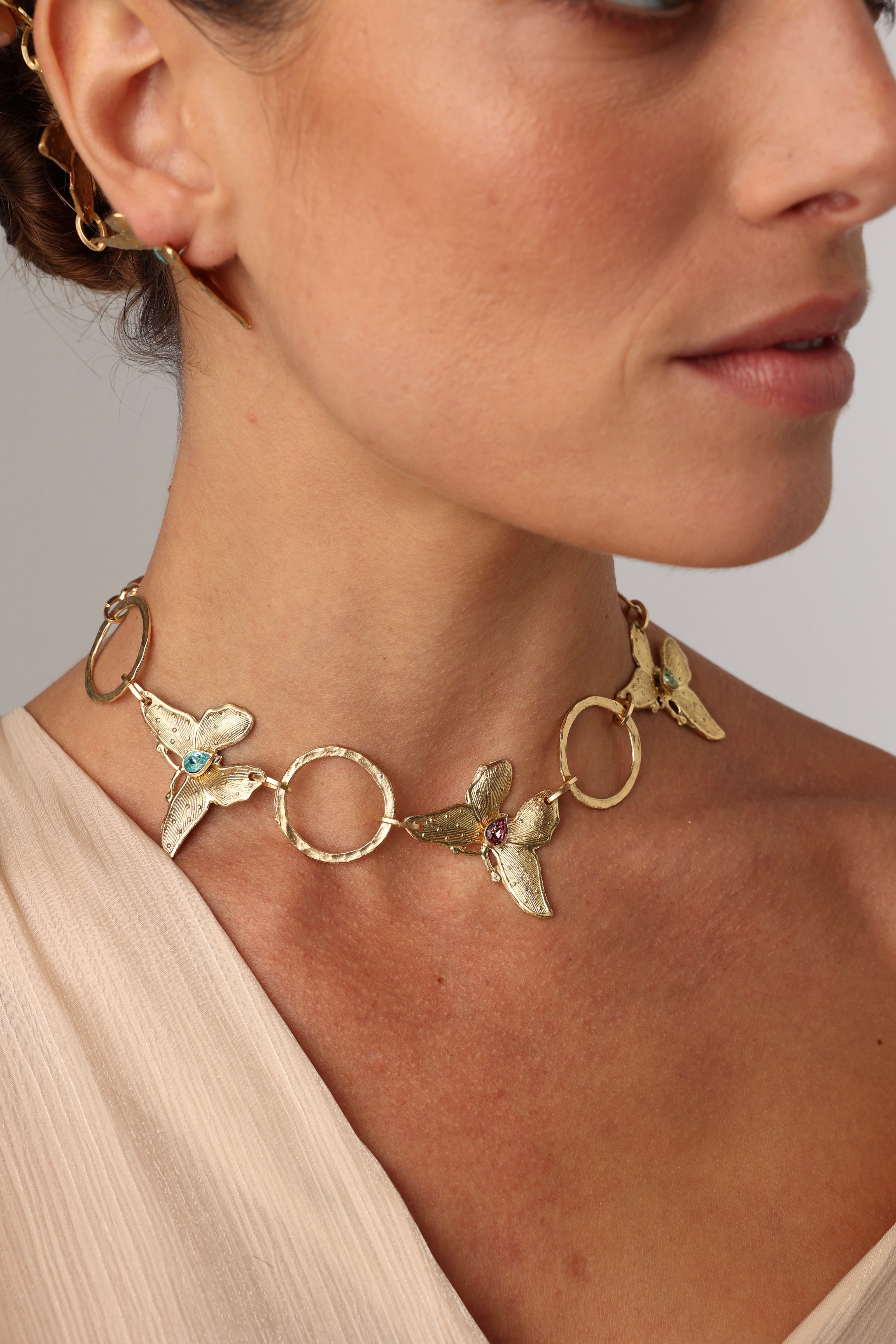 Nymia handmade brass butterfly choker necklace in gold with blue topaz and pink tourmaline worn on a model with a blush top