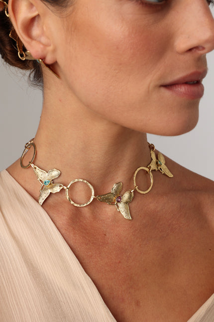 Nymia handmade brass butterfly choker necklace in gold with blue topaz and pink tourmaline worn on a model with a blush top