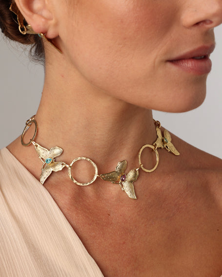 Nymia handmade brass butterfly choker necklace in gold with blue topaz and pink tourmaline worn on a model with a blush top