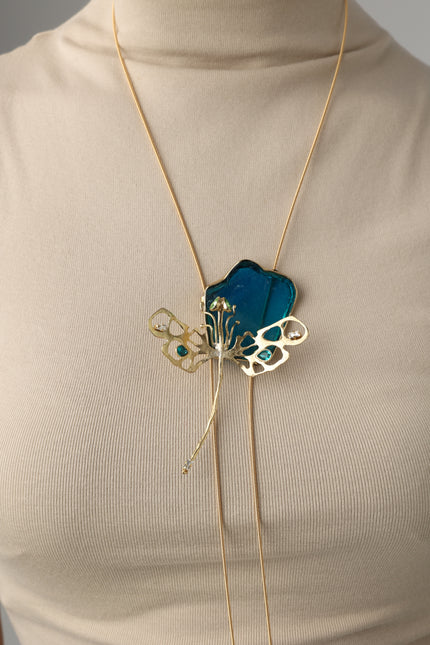 Zephyra handmade brass floral statement necklace with blue resin flower and crystals on beige turtleneck mannequin