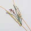 Close-up flat lay of Fiora gold lariat necklace pendant with hand-enameled green reeds, purple enamel wildflowers, iridescent opal and faceted pink tourmaline