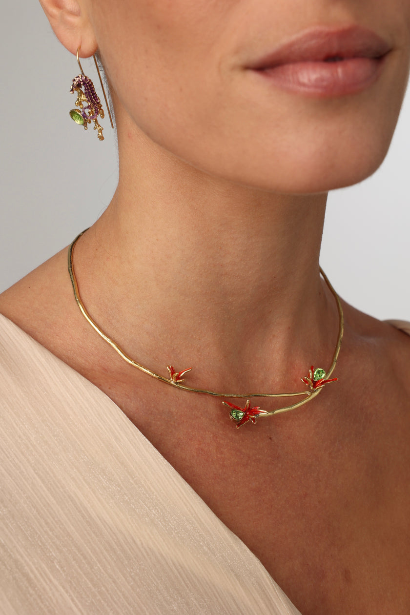 Close-up of a woman wearing a gold necklace with floral designs and green gemstones.